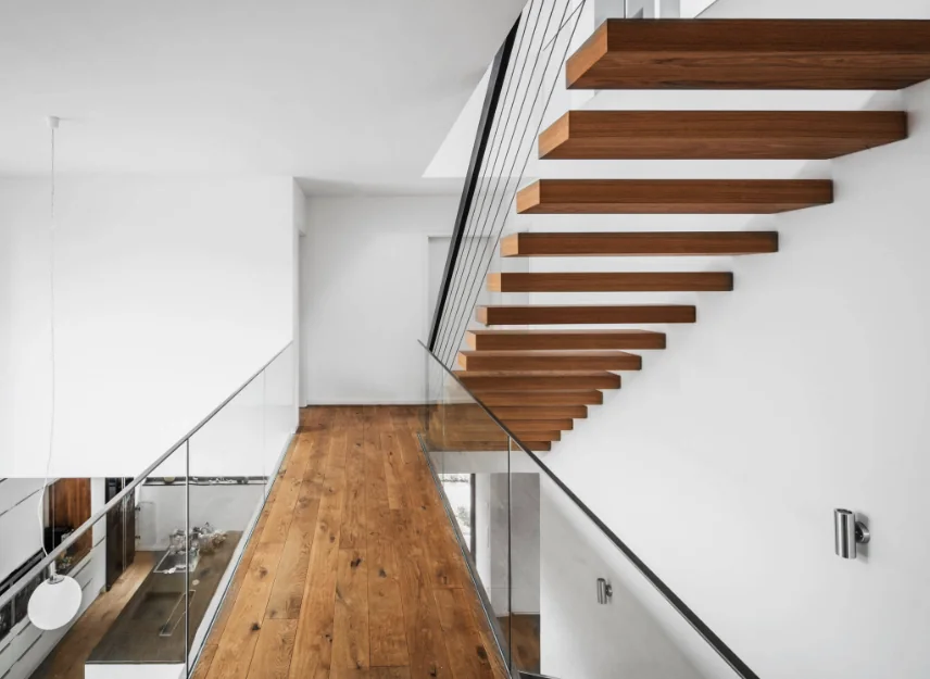 Heller Wohnbereich mit Holzbelag, Glaskonstruktion und frei schwebender Treppe