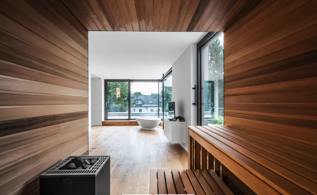 Wellnessbereich mit Holzverkleidung und Blick in ein helles Badezimmer mit freistehender Badewanne